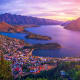 Aerial sunset view of Queenstown, New Zealand with Lake Wakatipu, surrounding mountains and forested hills at dusk